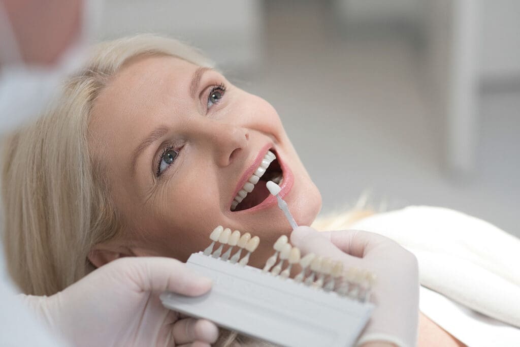 Dentist at East Lansing clinic uses shade guide to match a patient’s tooth color for potential veneers or whitening procedure.