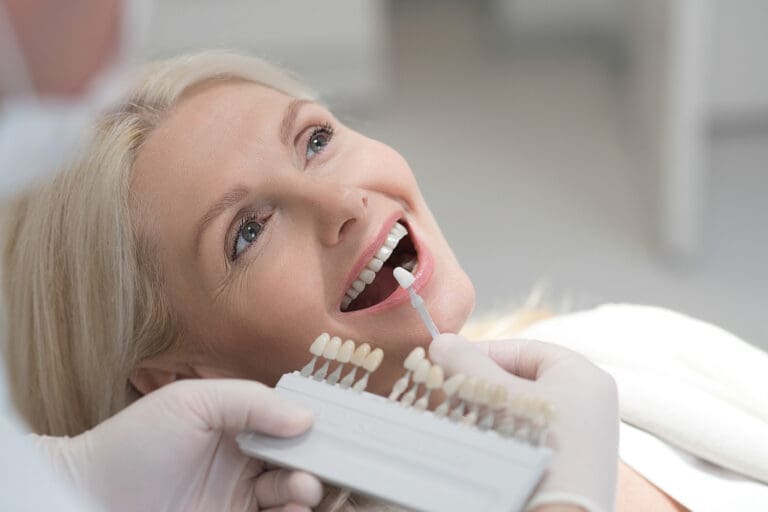 Dentist at East Lansing clinic uses shade guide to match a patient’s tooth color for potential veneers or whitening procedure.